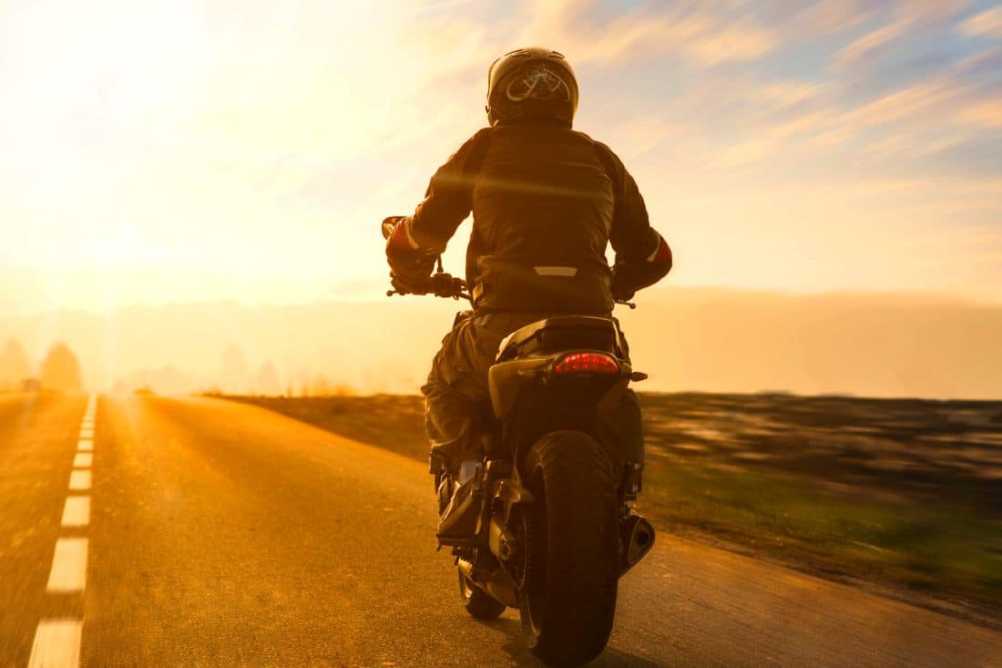 motorradfahrer mit helm auf abendlicher strasse im gegenlicht unterwegs