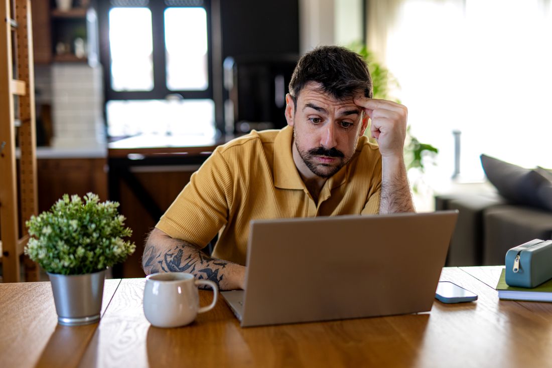 mann sitzt nach feierabend mit konzentriertem blick vor laptop am wohnzimmertisch