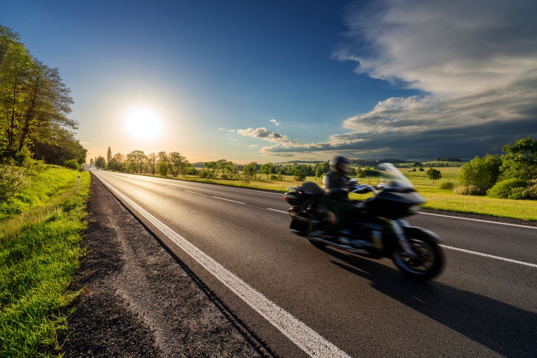 motorradfahrer faehrt bei tief stehender sonne ueber eine offene landstrasse im gruenen