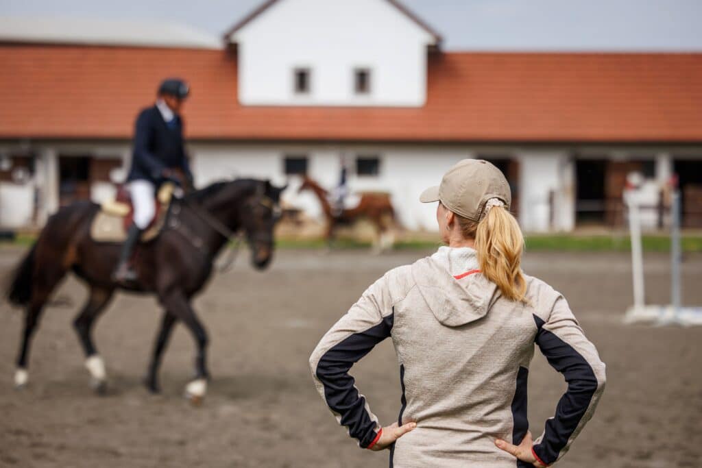 Trainer observing a rider during a training session, illustrating professional routines relevant to Show Jumping Horses for sale