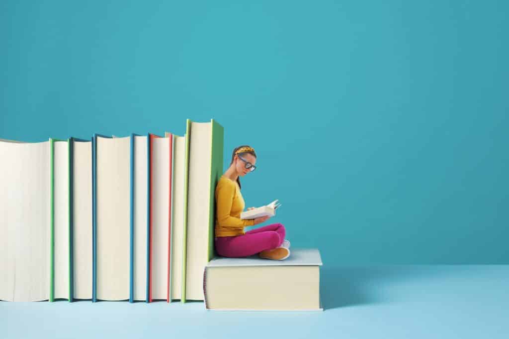 Frau liest inmitten großer Bücher | E-Learning Anbieter